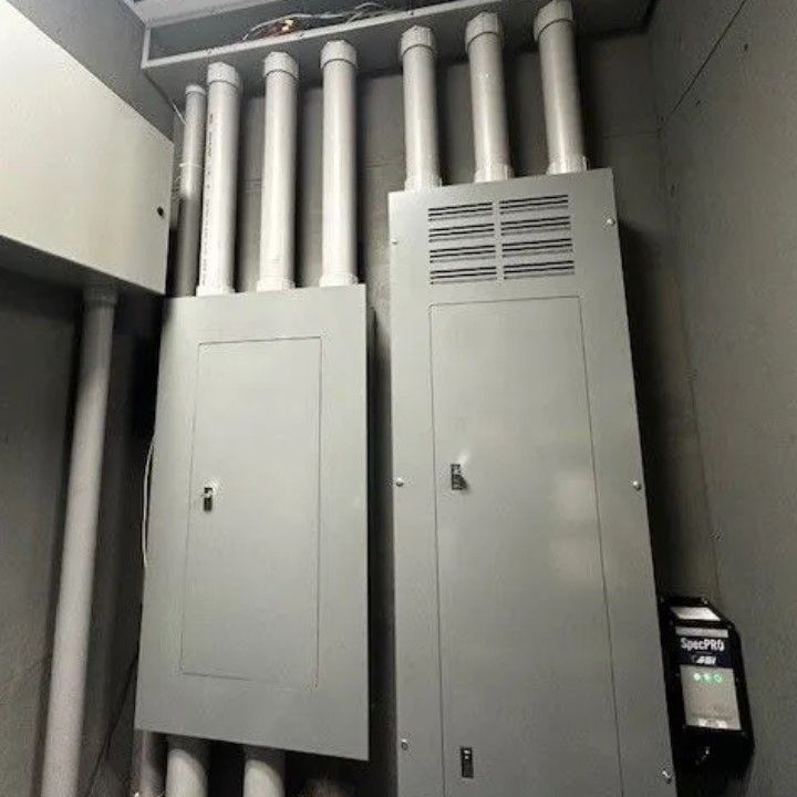 Two gray electrical panels with white conduits in a utility room.