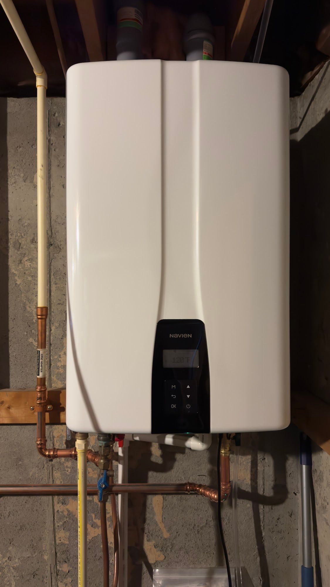 White tankless water heater on a wood-paneled wall, copper pipes visible.