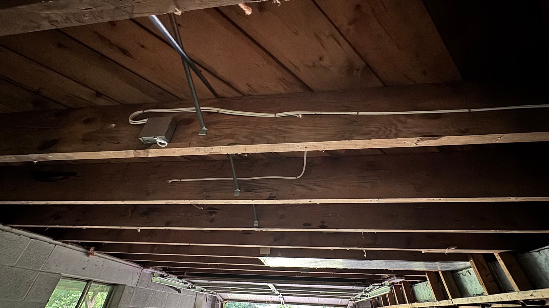 Wooden ceiling beams with electrical wiring, dark interior.