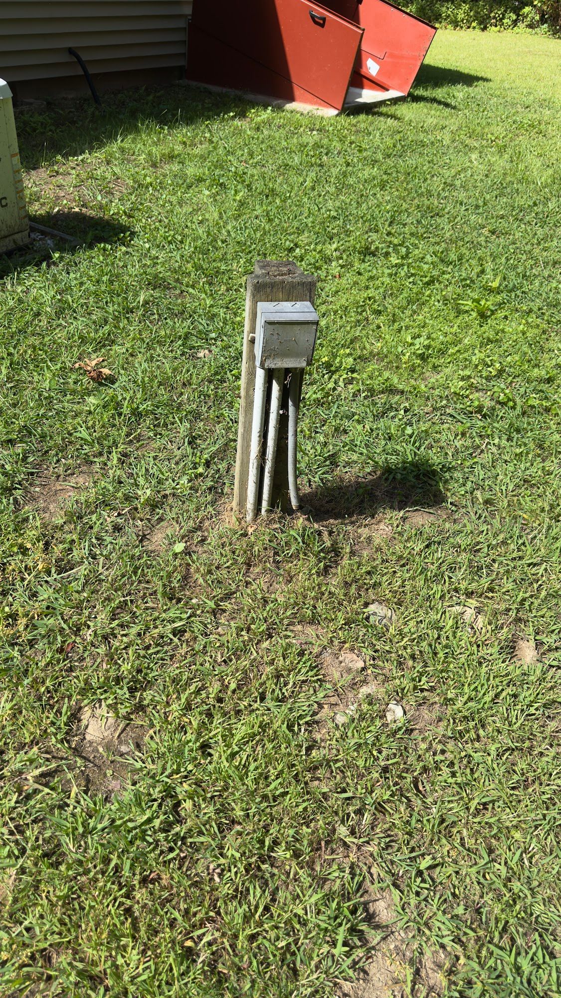 Electrical box on wooden post in grassy yard.