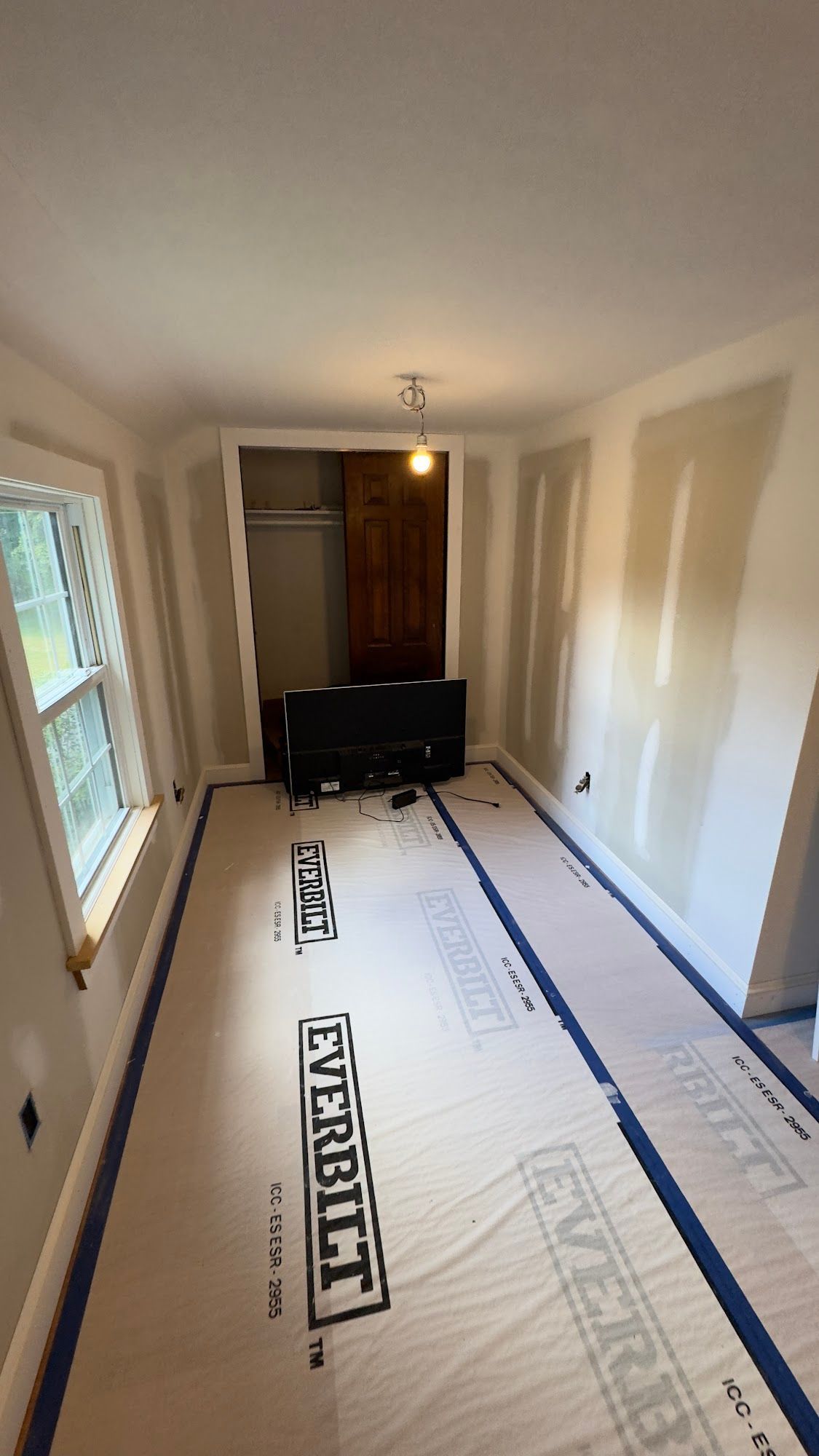 Room under construction with drywall and flooring.  Window on left, doorway in back.