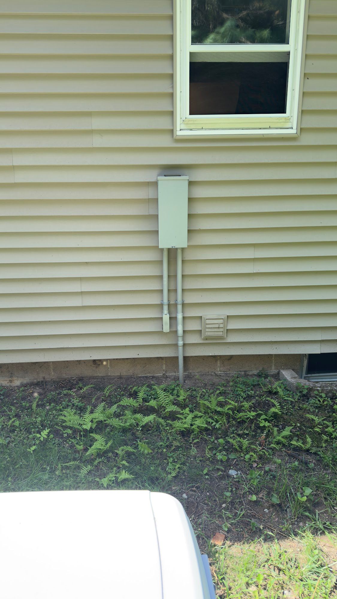Electrical box on beige siding with two conduits running down to the ground.