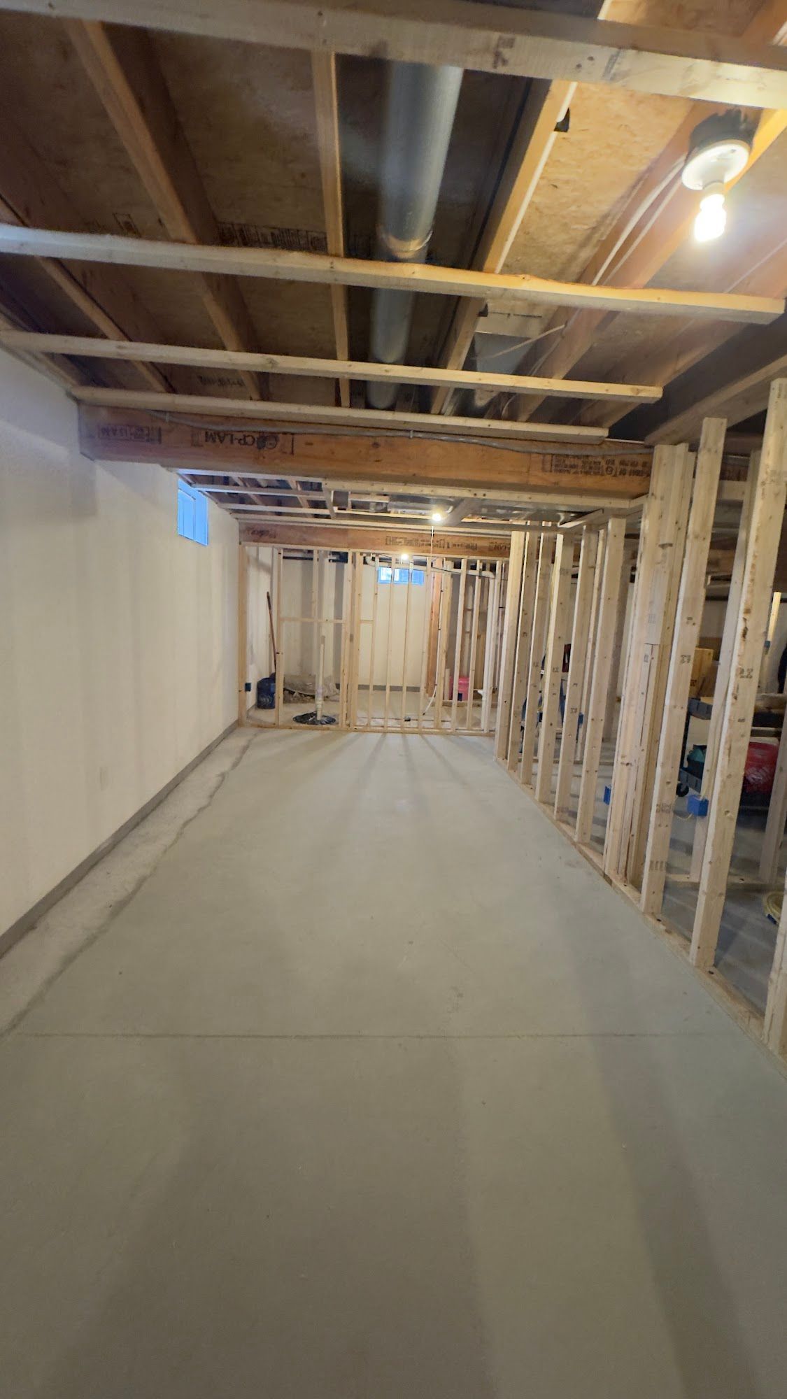 Basement under construction; exposed wood framing, concrete floor, white walls.