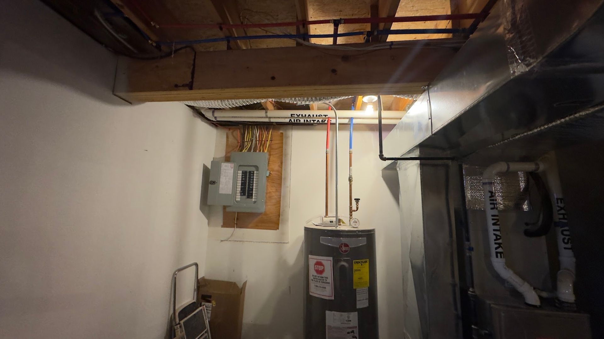 Basement with electrical panel, water heater, ductwork, and exposed pipes near ceiling.