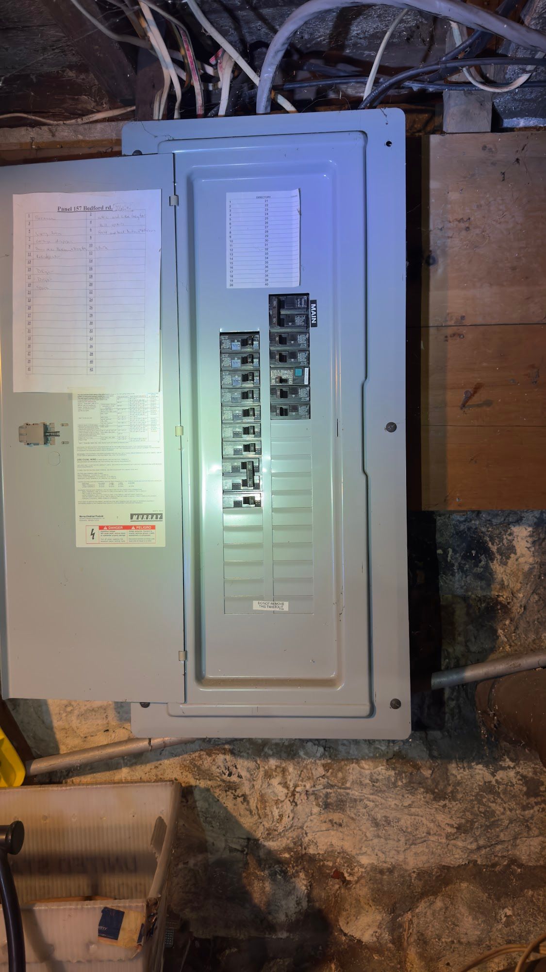 Electrical panel in a basement, with the panel door open, revealing circuit breakers and wiring.