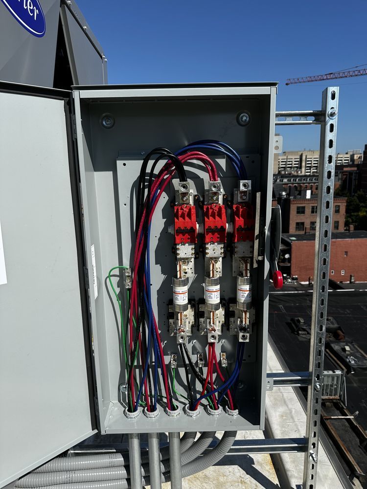 Open electrical box with wiring, red and white breakers, installed on a rooftop against a blue sky.