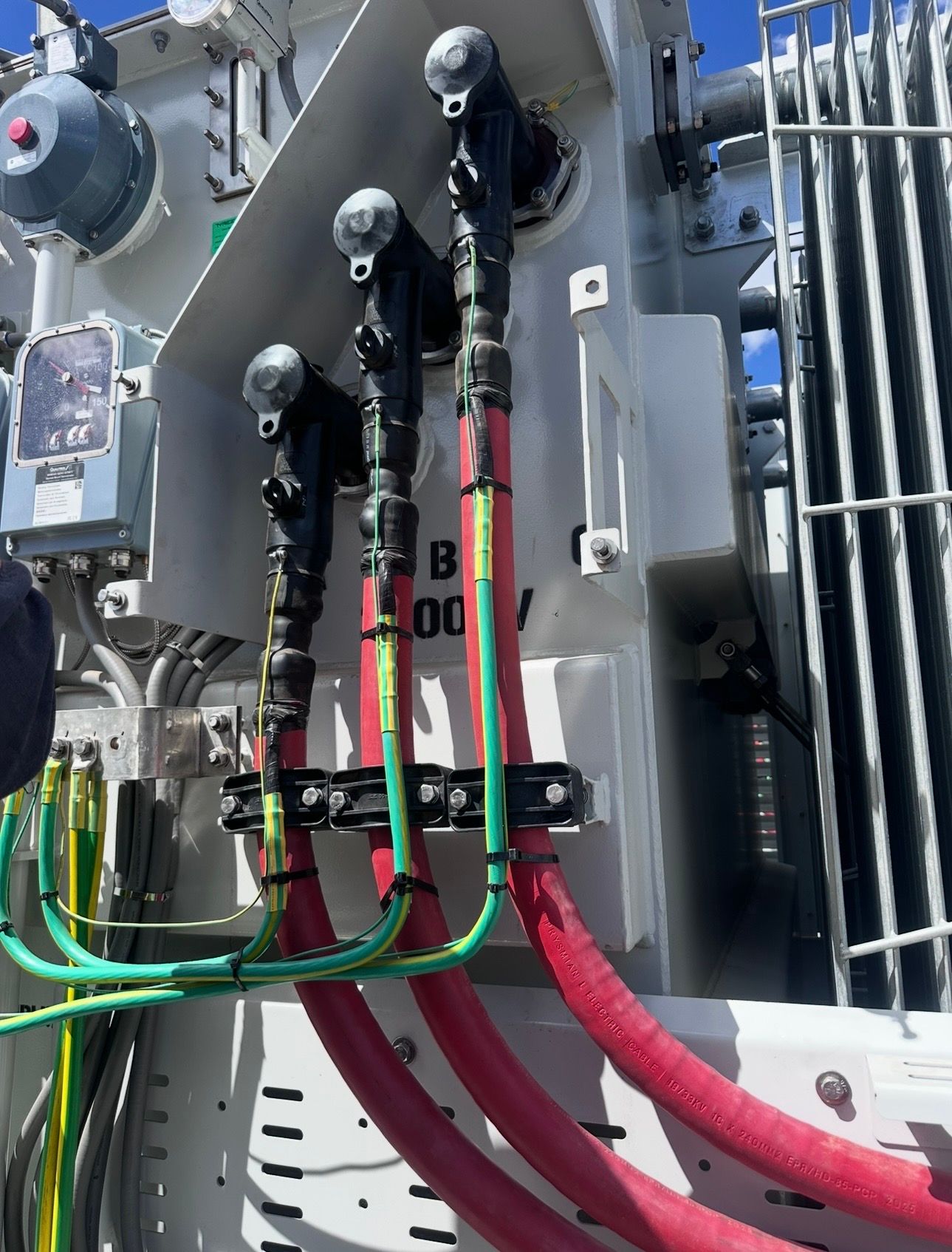 Electrical transformer with thick red and green cables connected outdoors