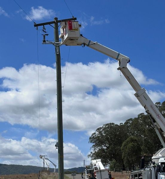 Utility workers in white boom lifts repairing a power pole under a blue sky