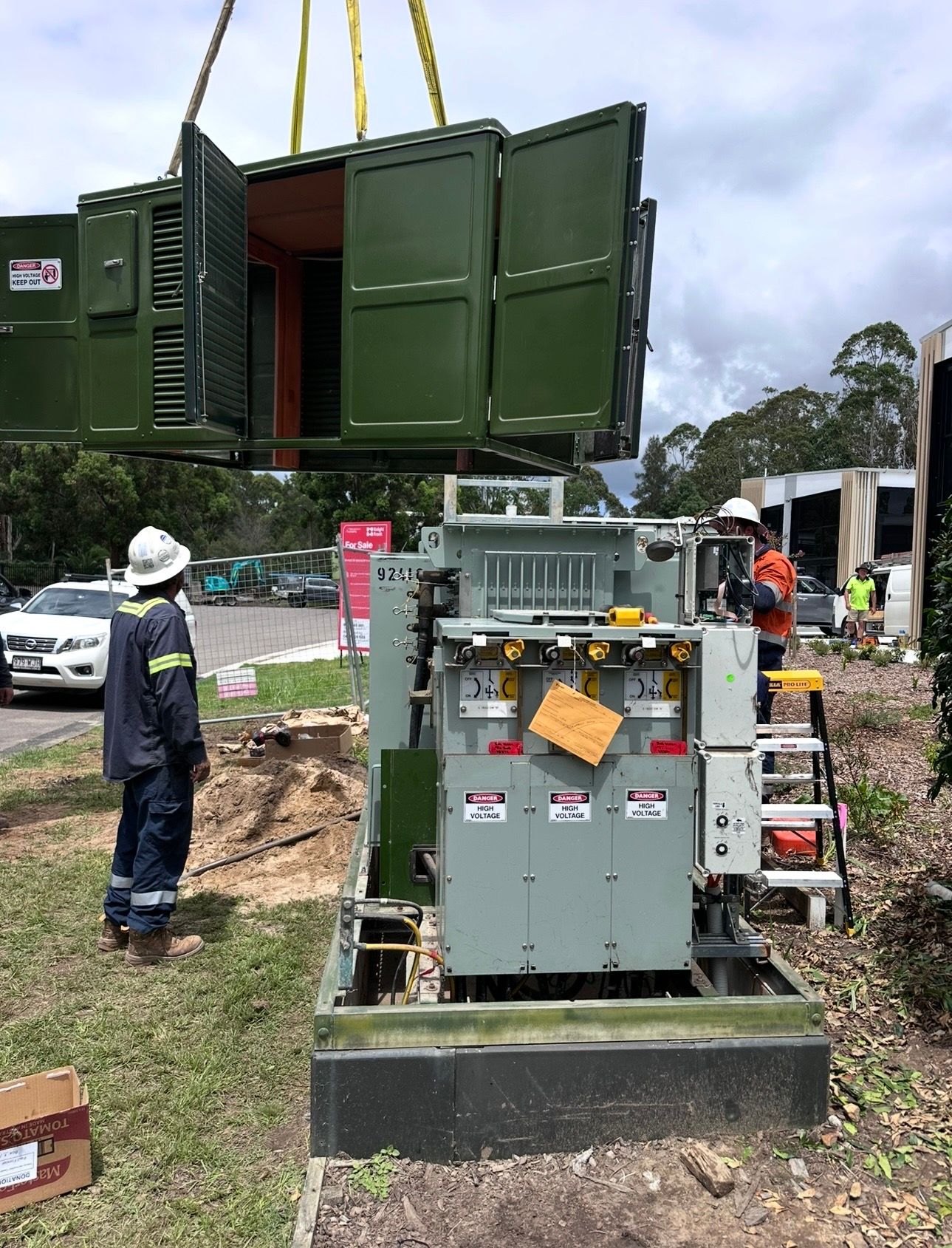 Workers beside a large green utility container and electrical equipment at an outdoor worksite