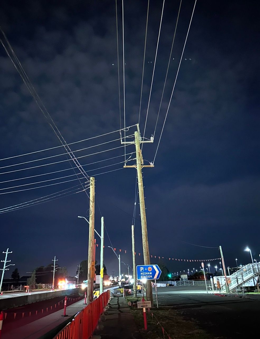 Nighttime street with utility poles and overhead power lines under a dark sky, lit by streetlights.