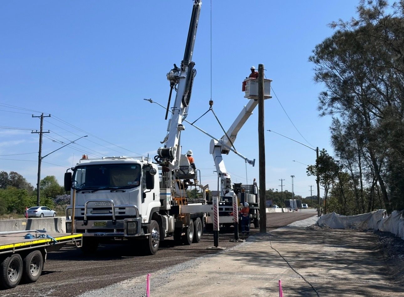 Utility trucks and bucket lifts working on power lines along a roadside construction area