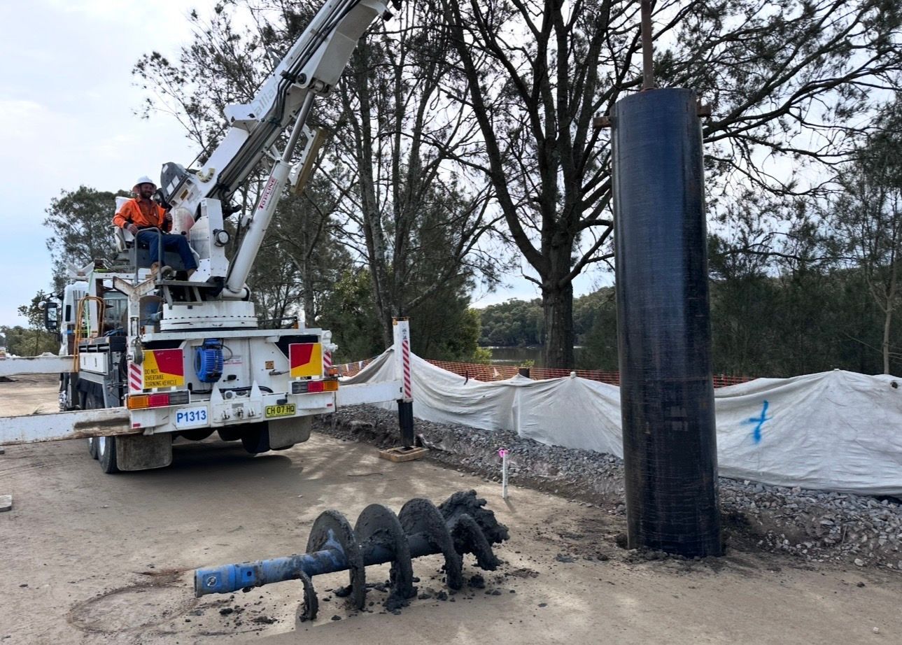 Utility truck with boom lift beside a large black pipe at a construction site