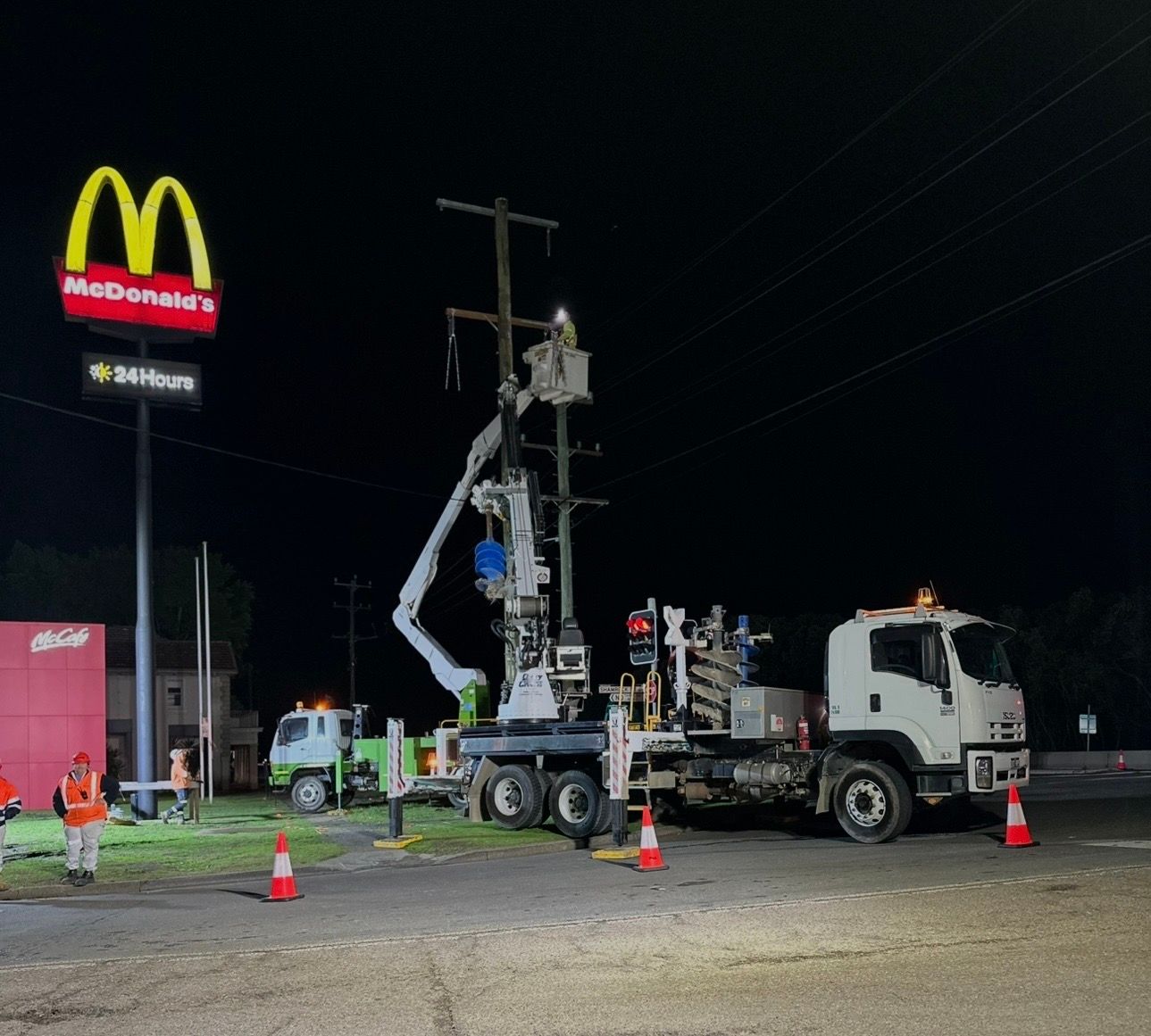 Utility truck working on power lines at night beside a McDonald’s, with cones and workers nearby