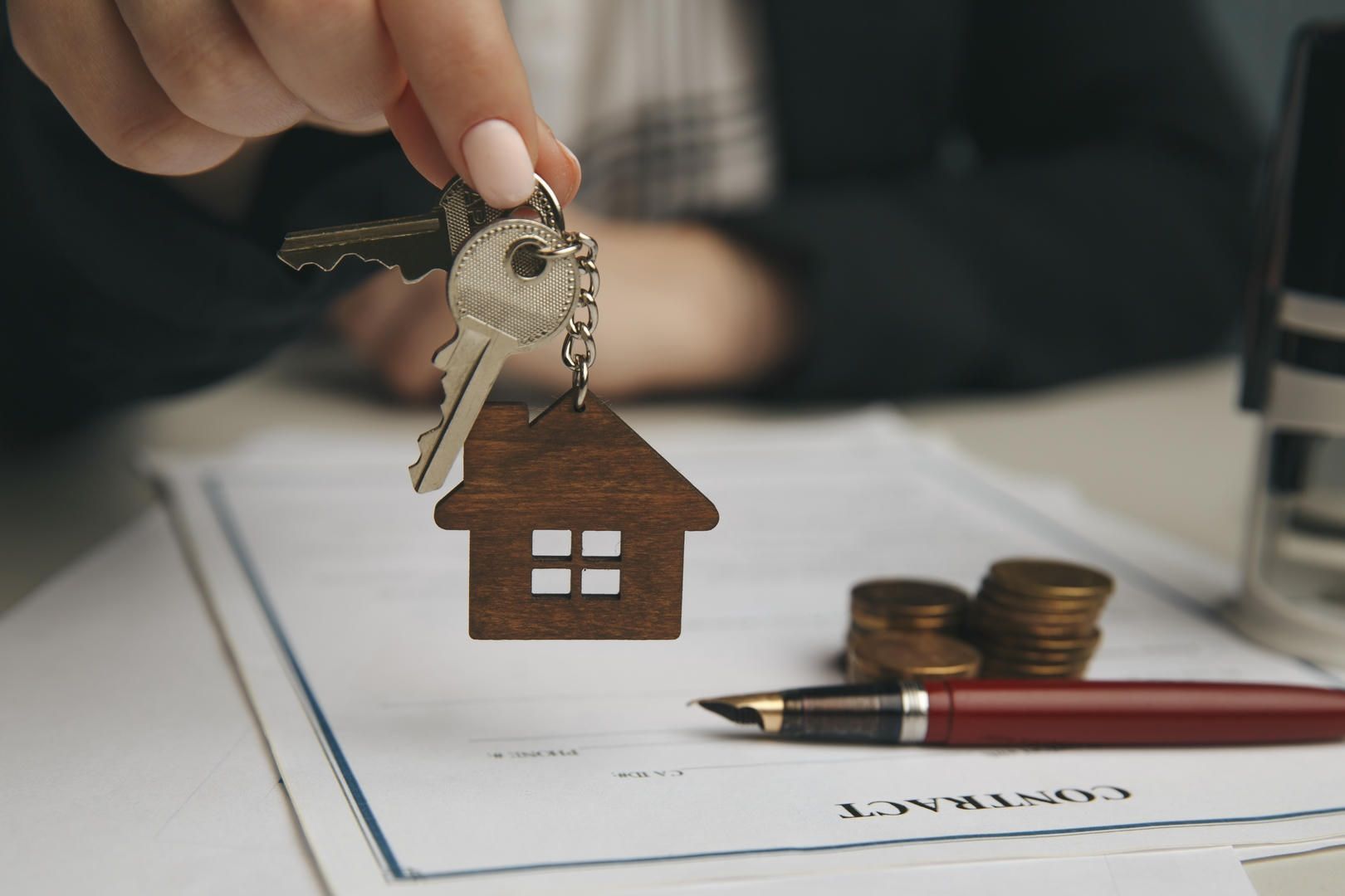 A woman is holding a pair of keys with a house keychain.