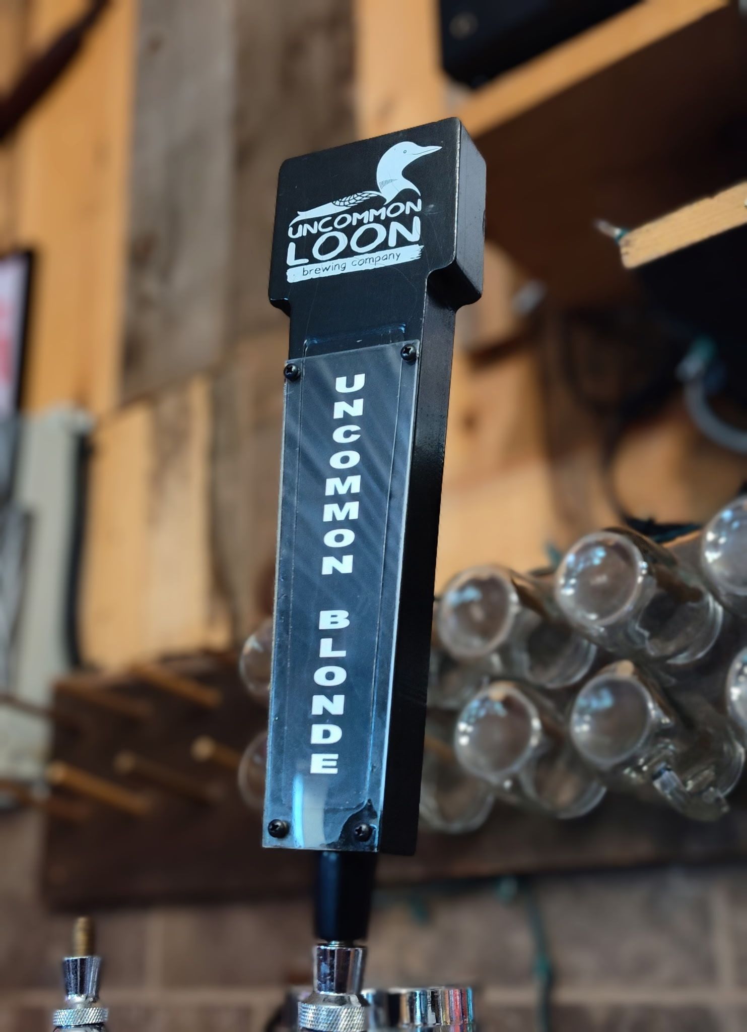 Black Moon gin tap handle with logo, mounted above a row of beer taps in a bar.