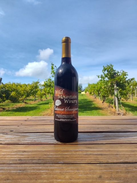 Wine bottle on a wooden table with vineyard rows and blue sky in the background