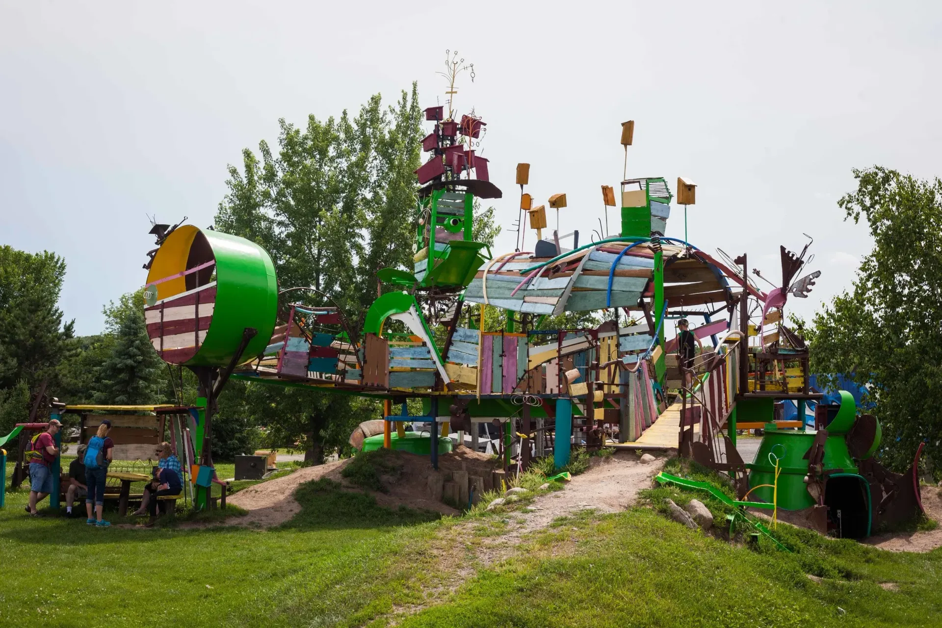 Colorful recycled art structure in a grassy park with people gathered around it