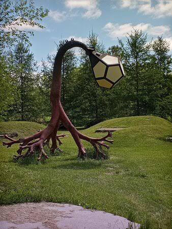 Abstract hexagonal lantern hanging from a twisted sculpture in a grassy park under a blue sky