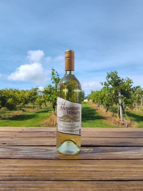 Wine bottle on a wooden table with a vineyard and blue sky in the background