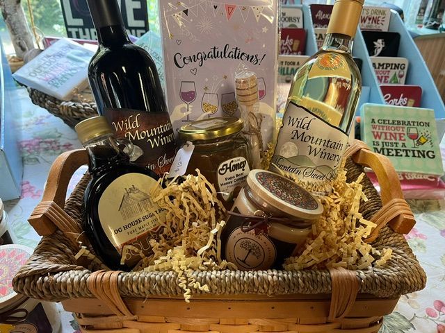 Gift basket with wine bottles, olive oil, spreads, and snacks in a wicker tray with straw filler.