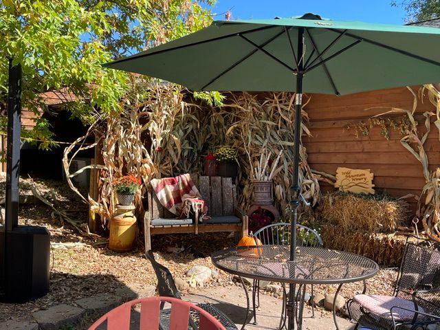 Patio with green umbrella, metal table, cushioned chair, and potted plants in a sunny garden corner