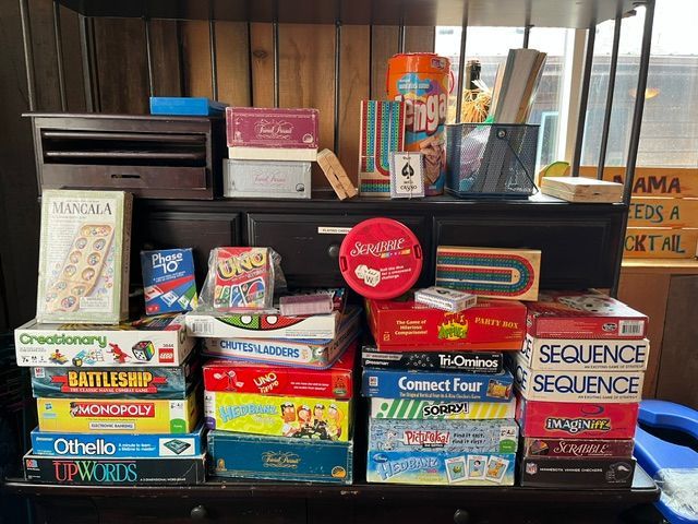 Stacked board games and boxes on a shelf, with colorful game titles visible.
