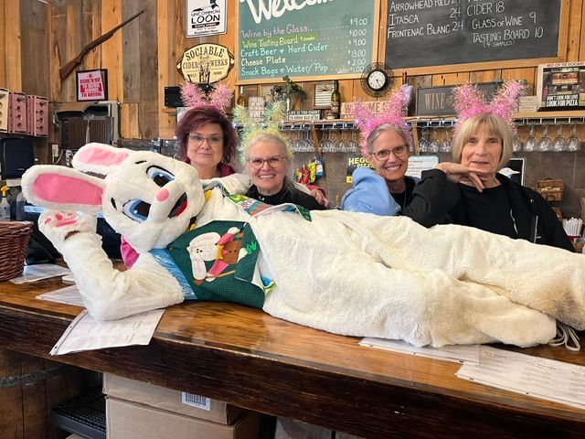 Four people pose behind a large white rabbit costume on a wooden table in a rustic cafe.