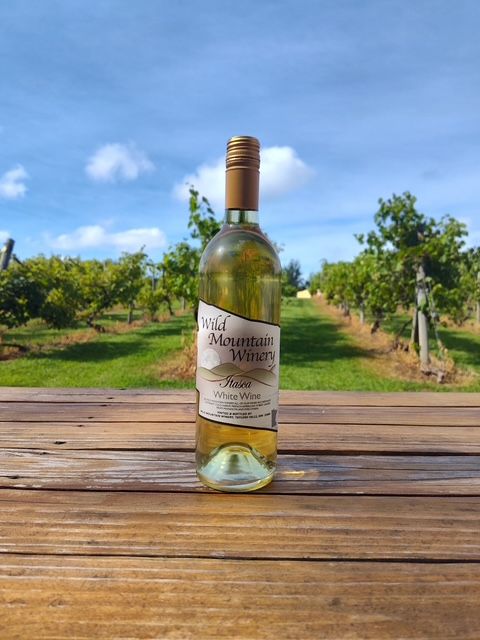 Wine bottle on a wooden table in a sunny vineyard with blue sky and green trees
