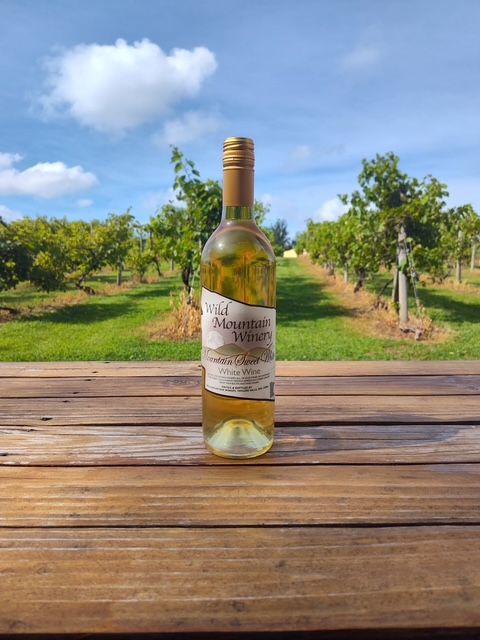 Wine bottle on a wooden table in an orchard under a blue sky
