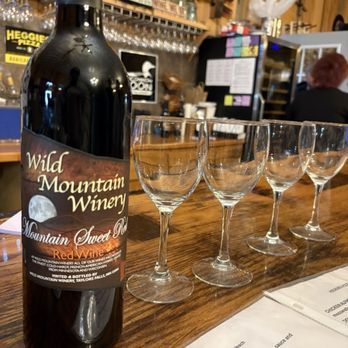 Bottle of Wild Mountain Winery red wine beside four empty wine glasses on a wooden bar counter