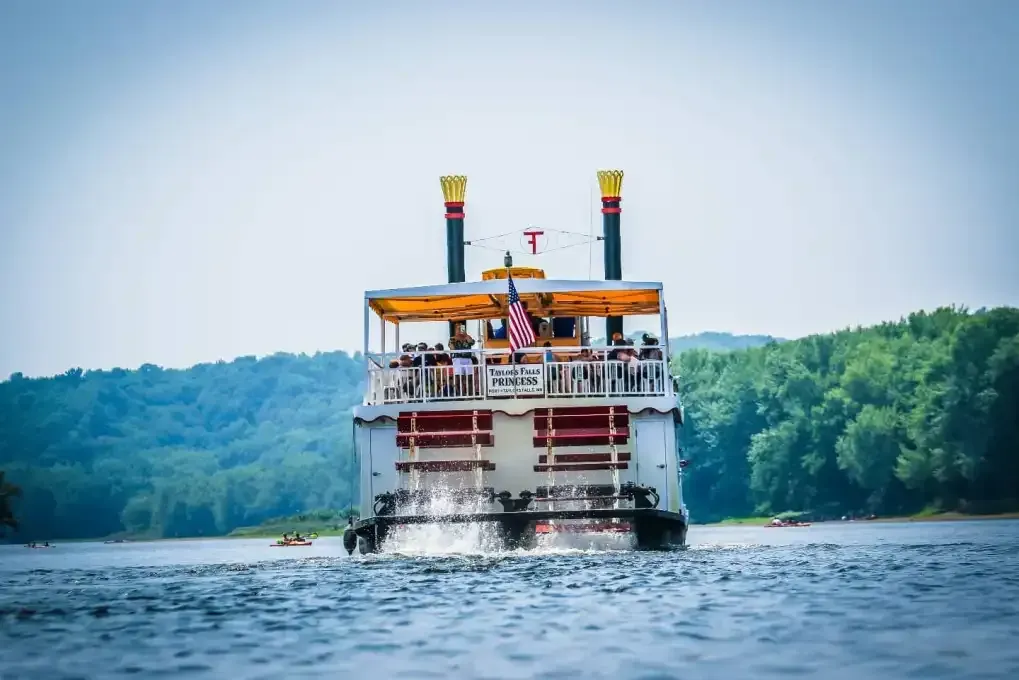 White riverboat cruising on blue water with trees and hills in the background