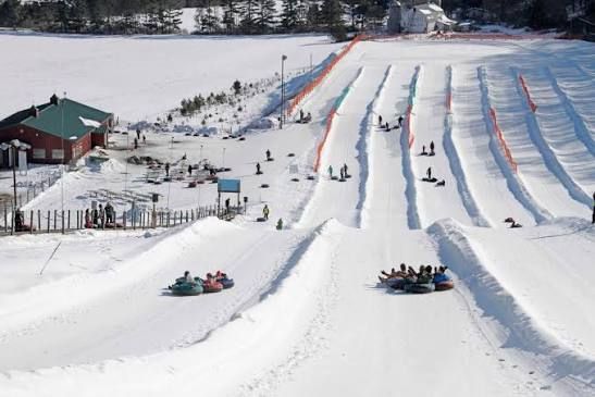 Snow tubing hill with multiple lanes, riders descending, and a lodge beside the slope