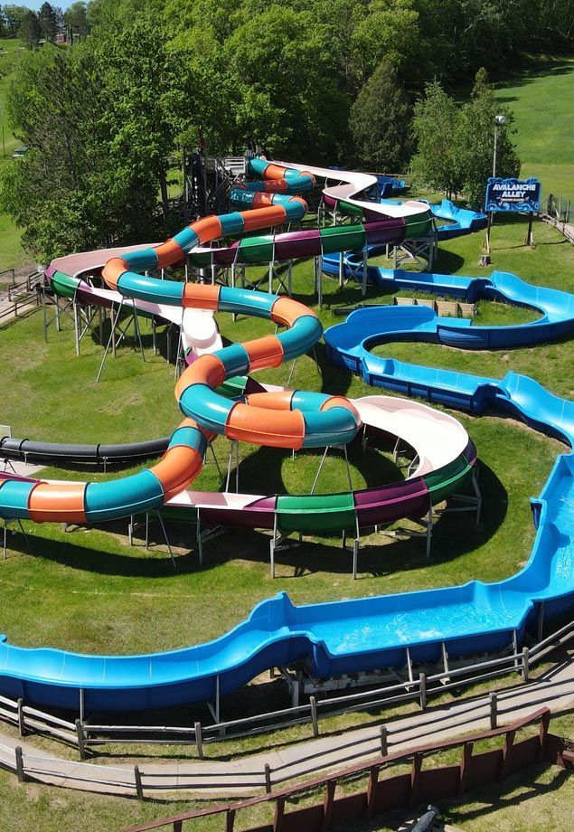 Colorful waterslide winding through a green outdoor water park, with blue pools and orange tubes