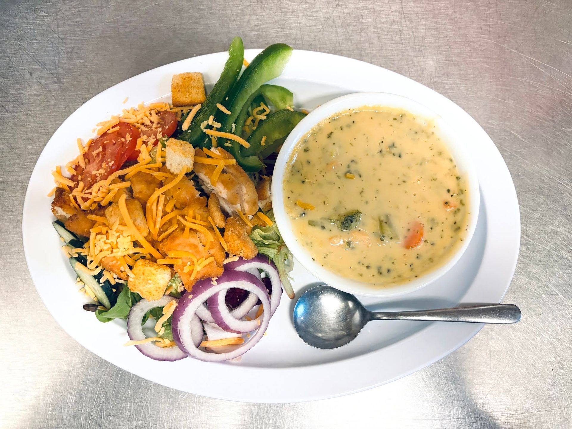 Salad and creamy soup on a white plate with a spoon on a stainless-steel table