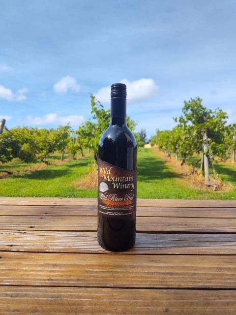 Wine bottle on a wooden table with a vineyard and blue sky in the background