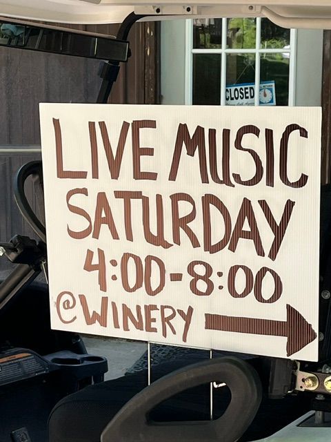 Sign advertising live music Saturday 4:00–8:00 at a winery, with an arrow pointing right