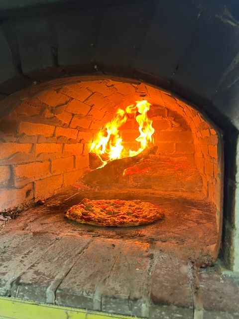 Wood-fired brick oven with blazing flames and a pizza baking on the hearth