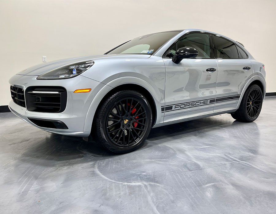 Silver Porsche Cayenne SUV with black accents and wheels, parked in a showroom.