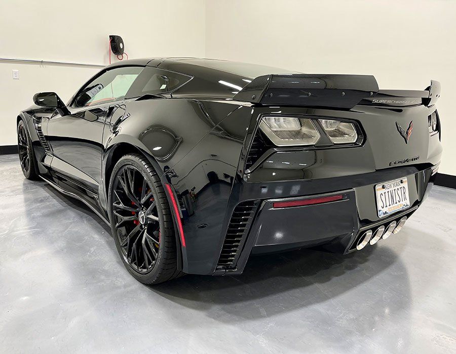 Black Corvette sports car, rear view, parked indoors, black wheels, red accents.
