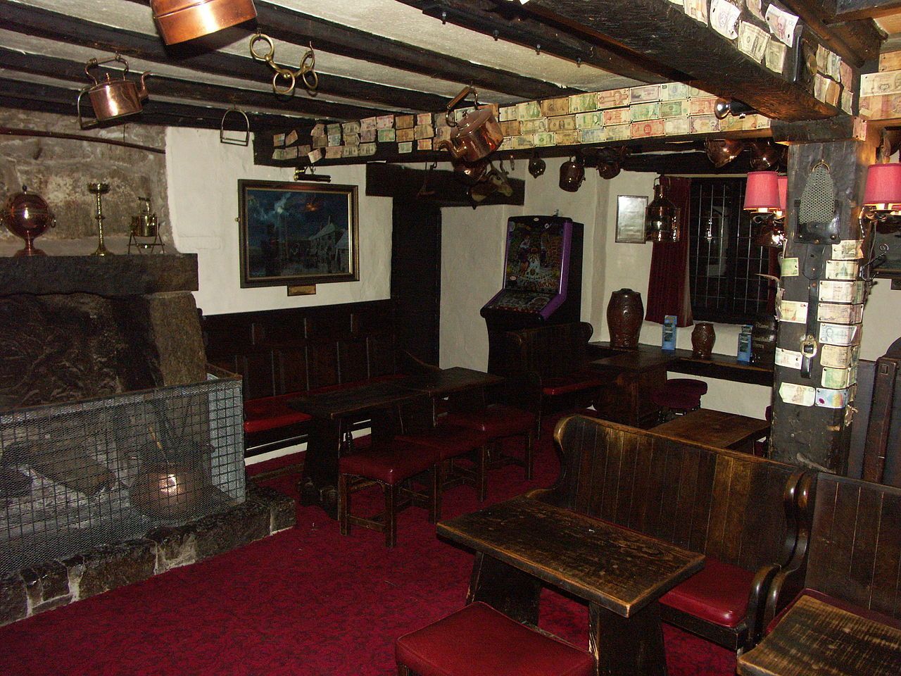 Interior of a traditional pub, dark wood furniture, fireplace, red carpet, and low ceiling.