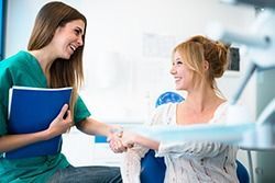 Two women smiling and shaking hands in a bright office, one holding a blue folder