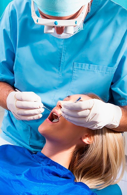 Dentist examining a patient during a dental checkup, with gloved hands and blue clinical attire.