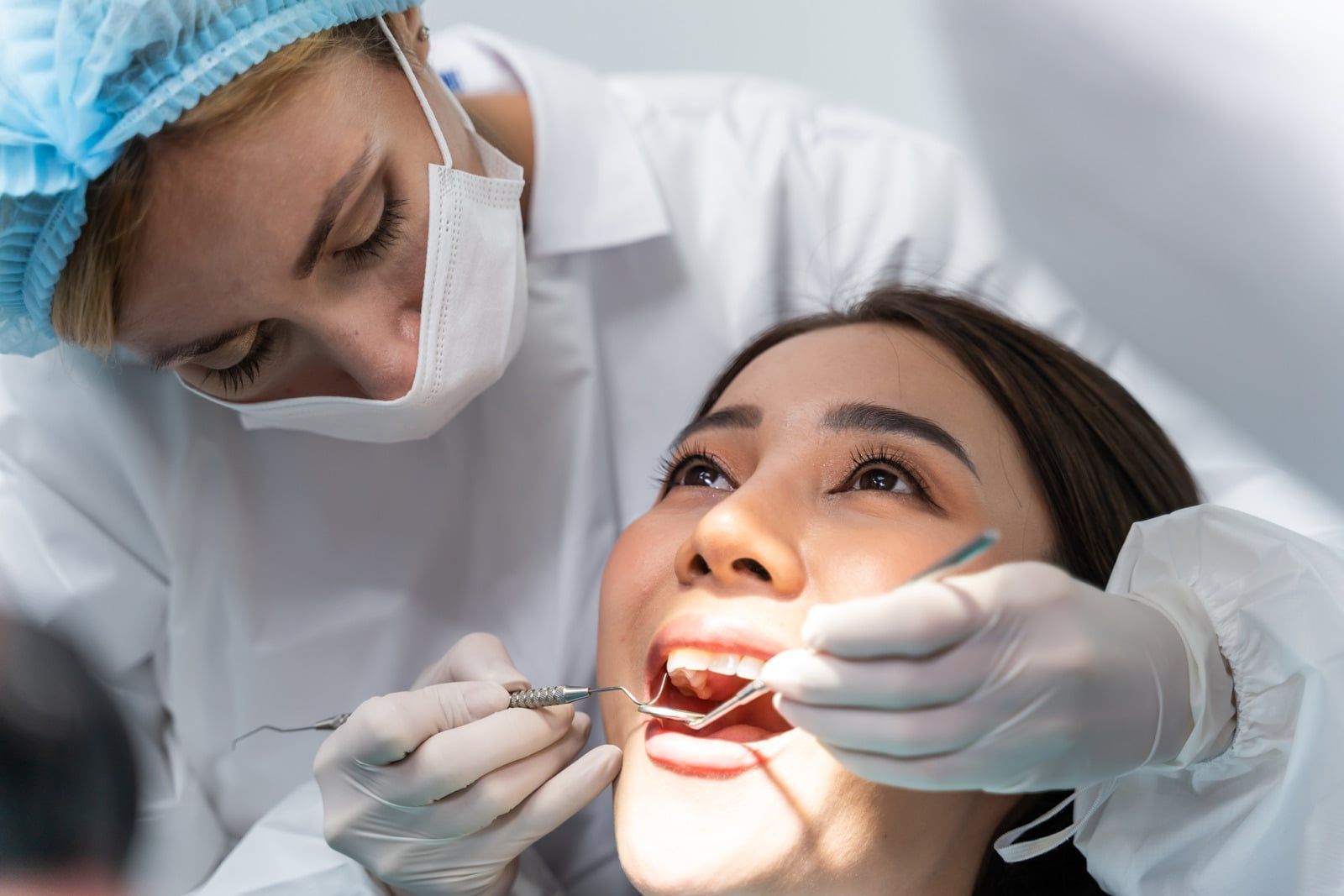 Dentist examining a patient during a dental checkup, with gloved hands and blue clinical attire.
