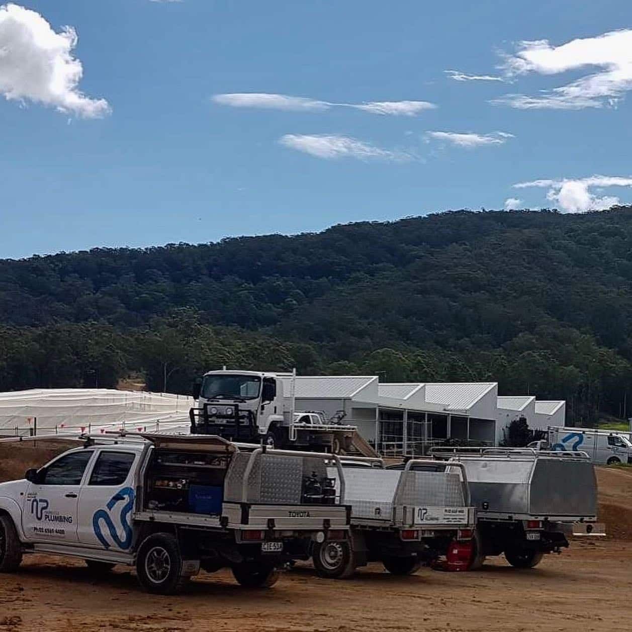 A Row of Trucks Parked in A Dirt Field with Mountains in The Background — Nambucca Plumbing in Nambucca Heads, NSW