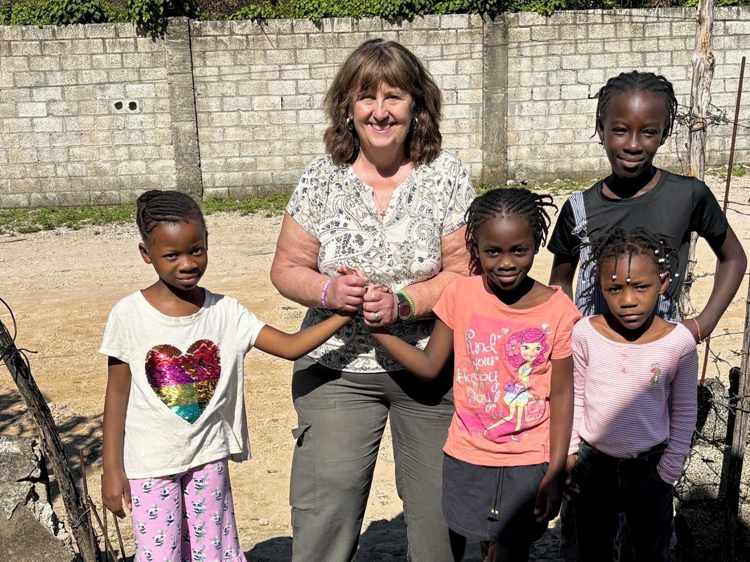 Five children and an adult standing outdoors in front of a stone wall, smiling at the camera.
