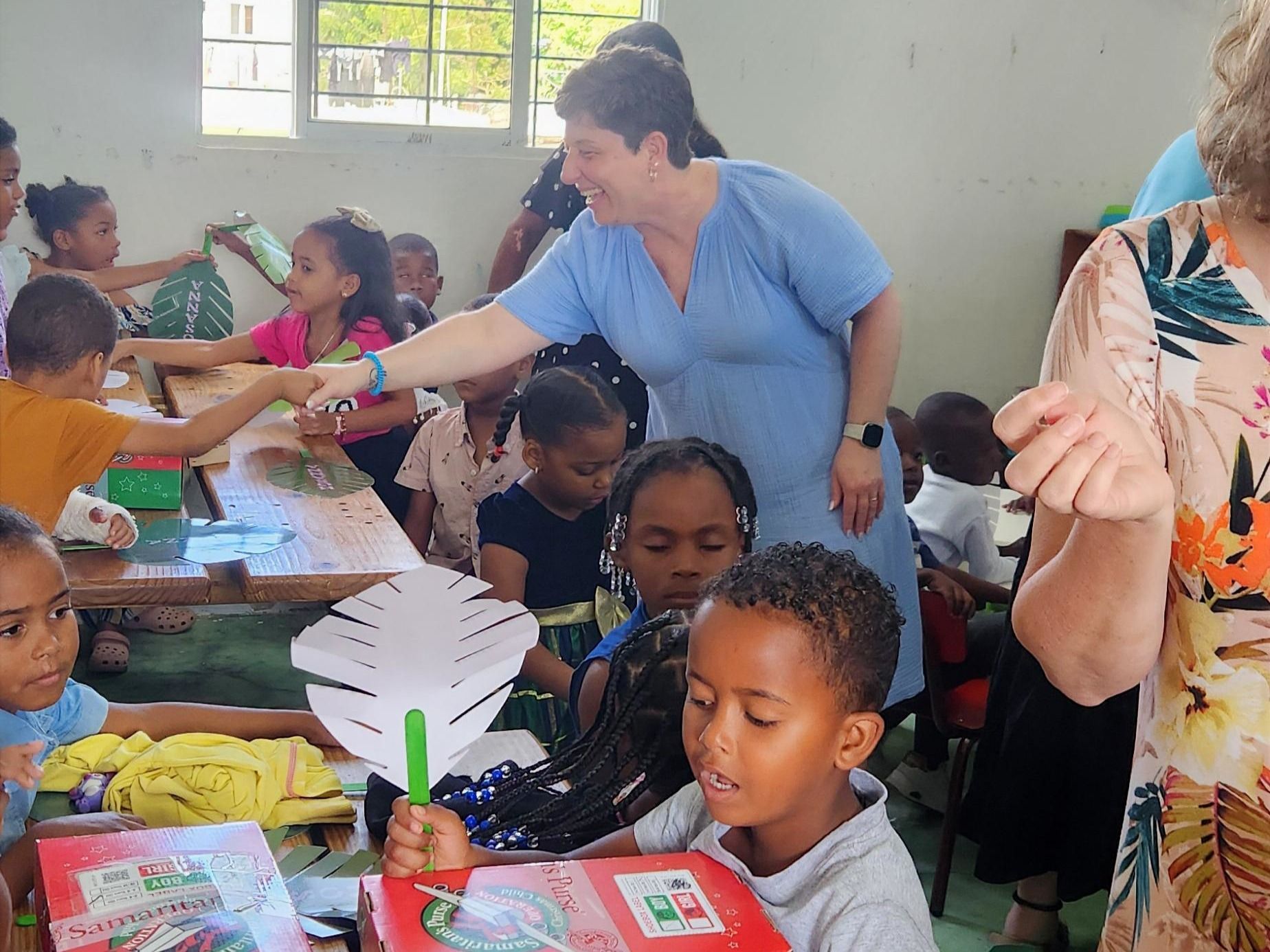 An adult handing out materials to children at a classroom table during a group activity