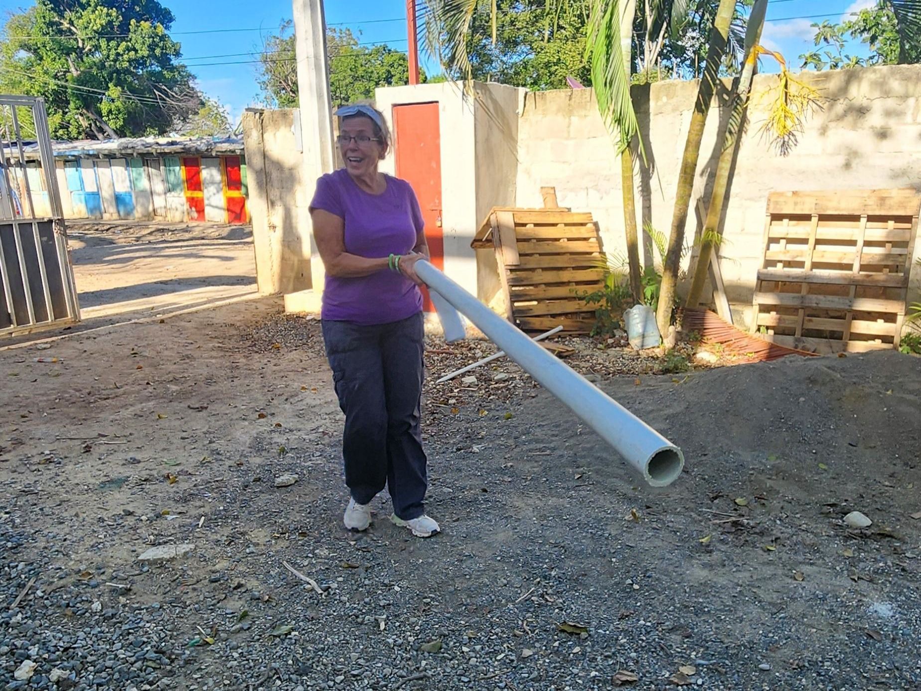 An adult in a purple shirt holding a long white pipe outdoors on a gravel lot.