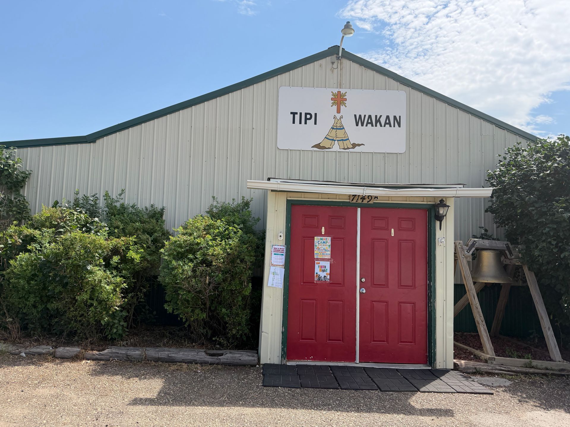 Red double doors on a metal building with a TPI Hawan sign and bushes at the entrance