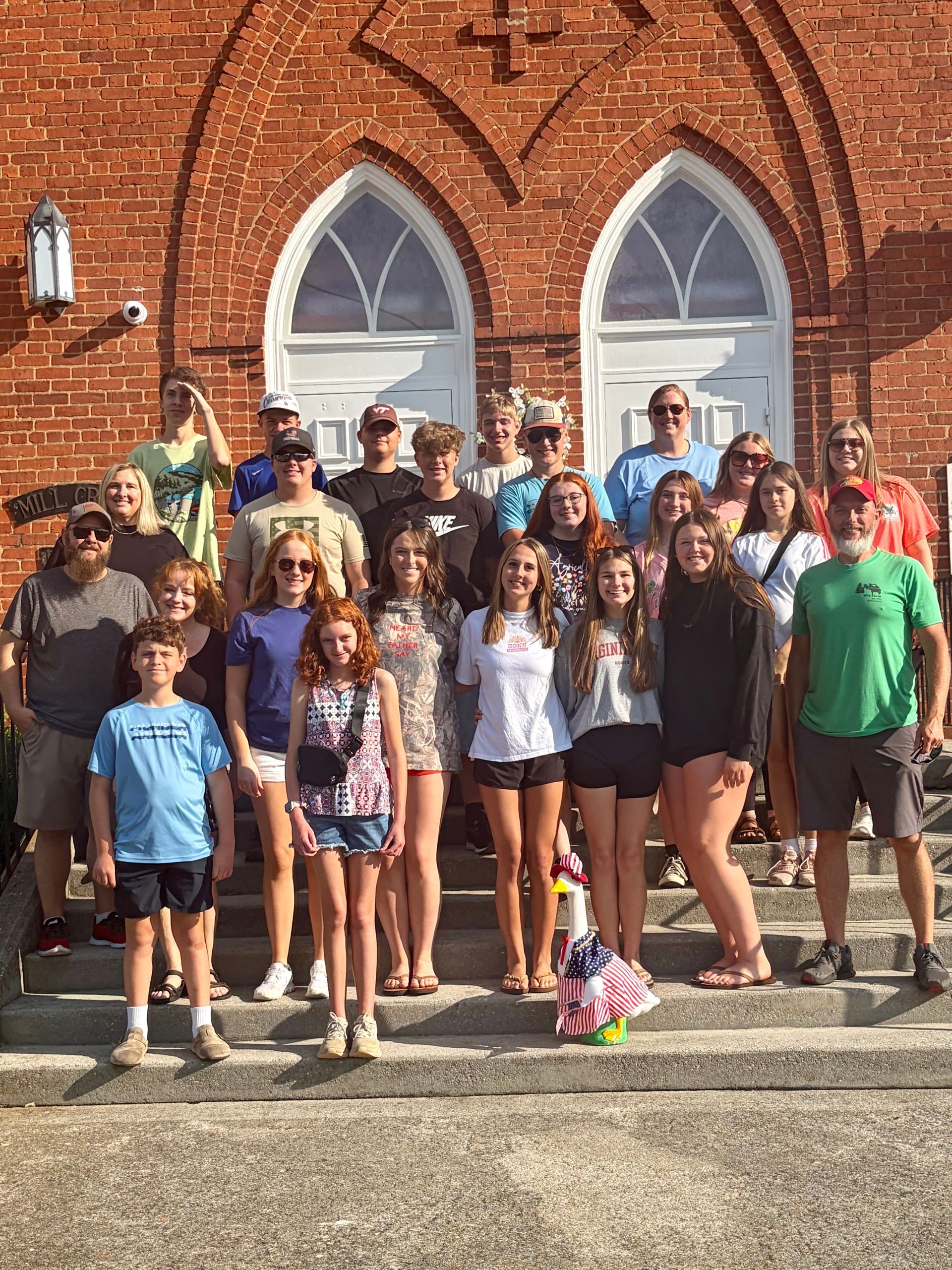 Group of teenagers posing on steps in front of a brick church with arched windows