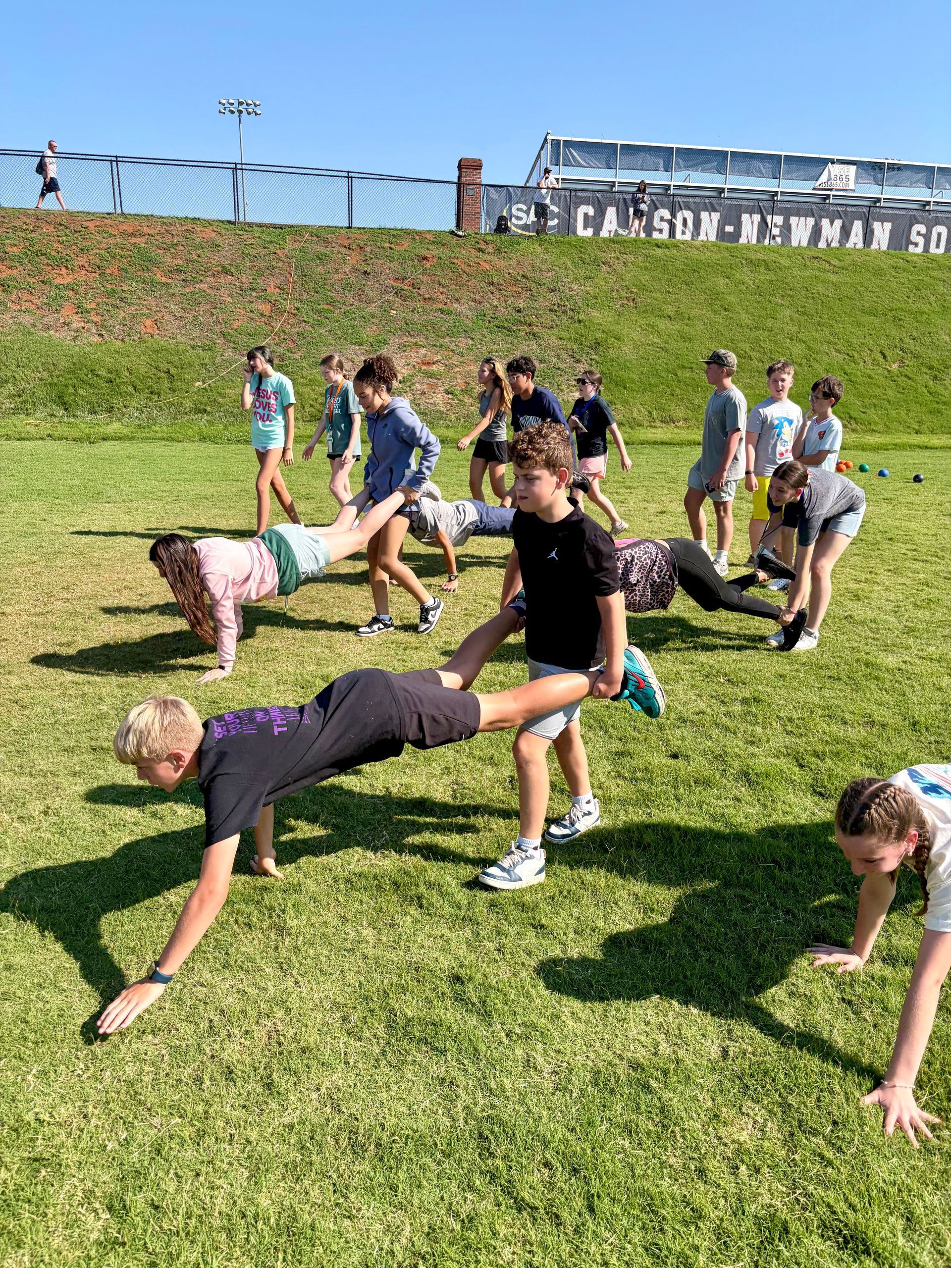 Teenagers doing outdoor games and activities on a grassy field under bright sunlight